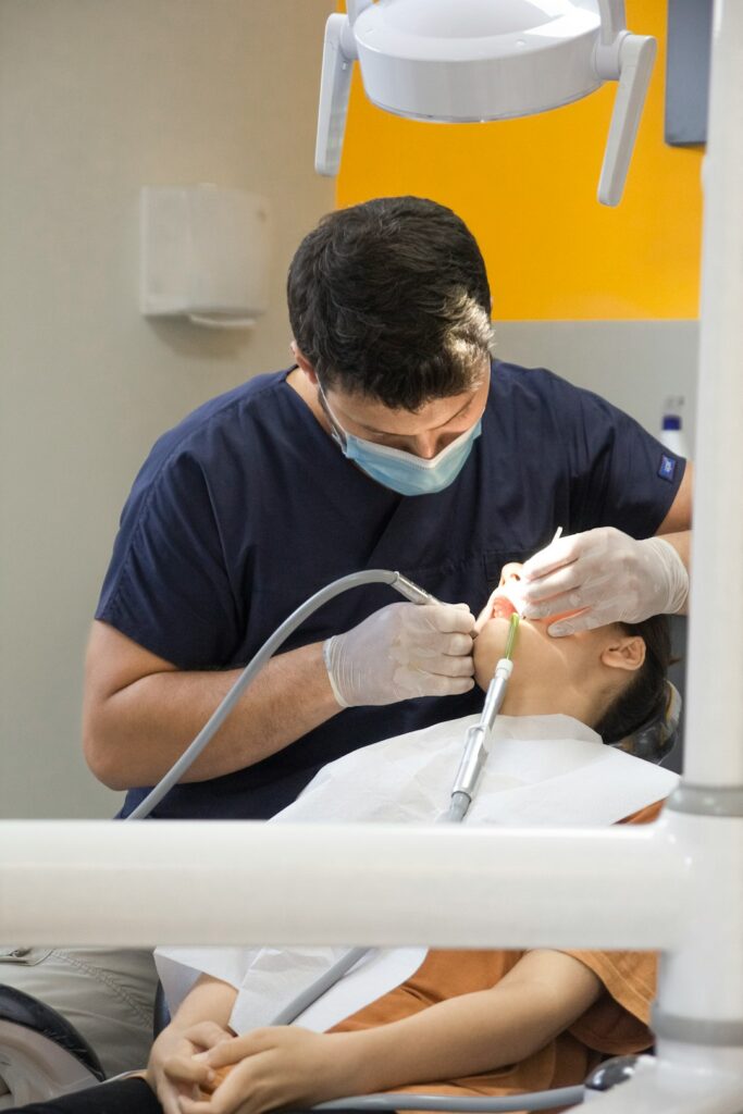 Patient in a dental chair receiving care while an implant treatment plan is reviewed on a monitor.