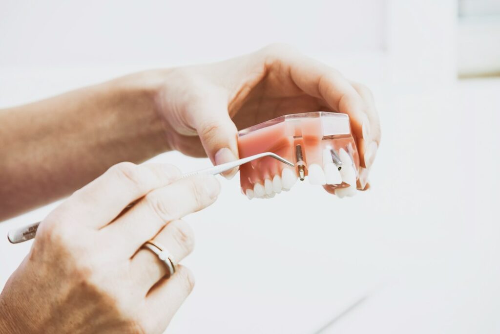 Adult examining a dental model comparing a removable denture with an implant-supported tooth on a clinic table.