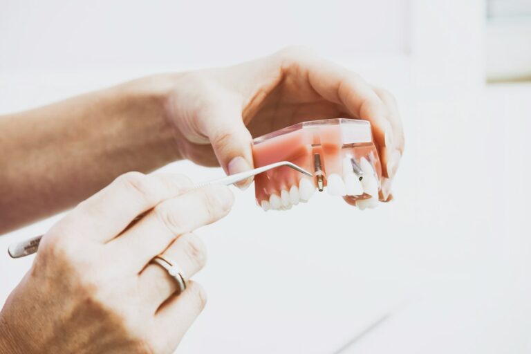 Adult examining a dental model comparing a removable denture with an implant-supported tooth on a clinic table.
